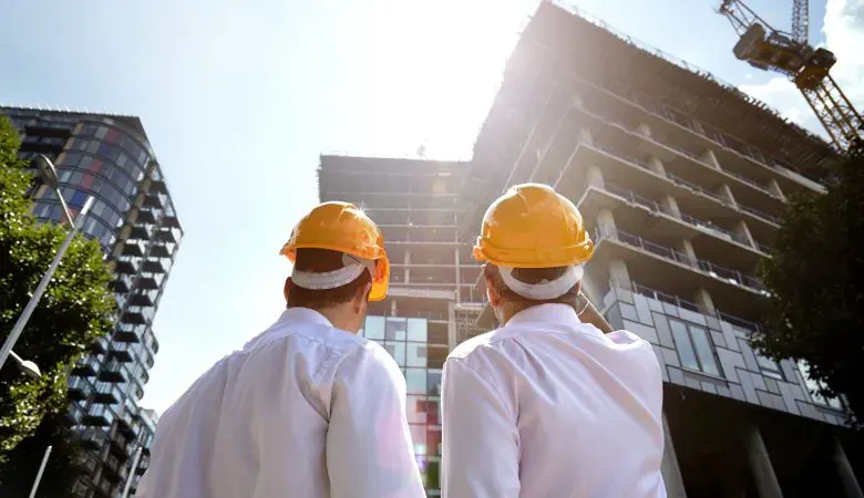 Dois profissionais de capacete olhando um edifício em construção