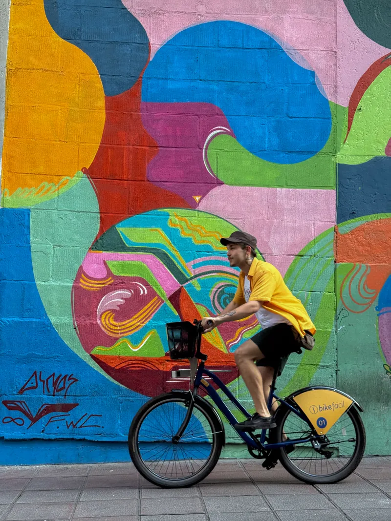 Ciclista usando uma bicicleta compartilhada Bike Fácil diante de um mural colorido